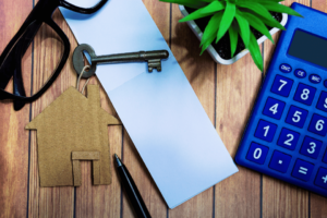 Image shows notepad with house model and key on wooden desk